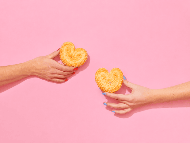 Dos manos brindan con orejitas sobre un fondo rosado.